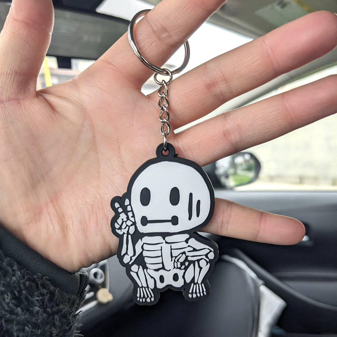 hand holding a skeleton skelemen black and white rubber strap keychain