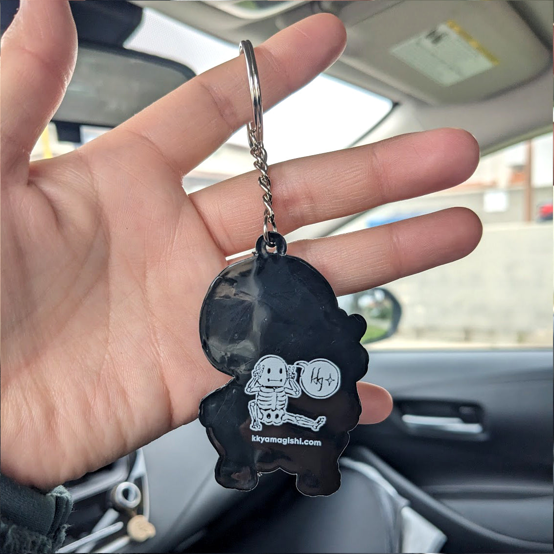 hand holding a skeleton skelemen black and white rubber strap keychain showing the back view with logo